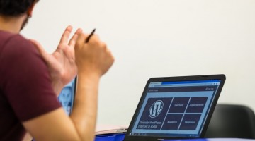 Taranto, Italy - July 19, 2019: Young student with pen in hand and laptop resting on desk, visible the WordPress logo on the screen.